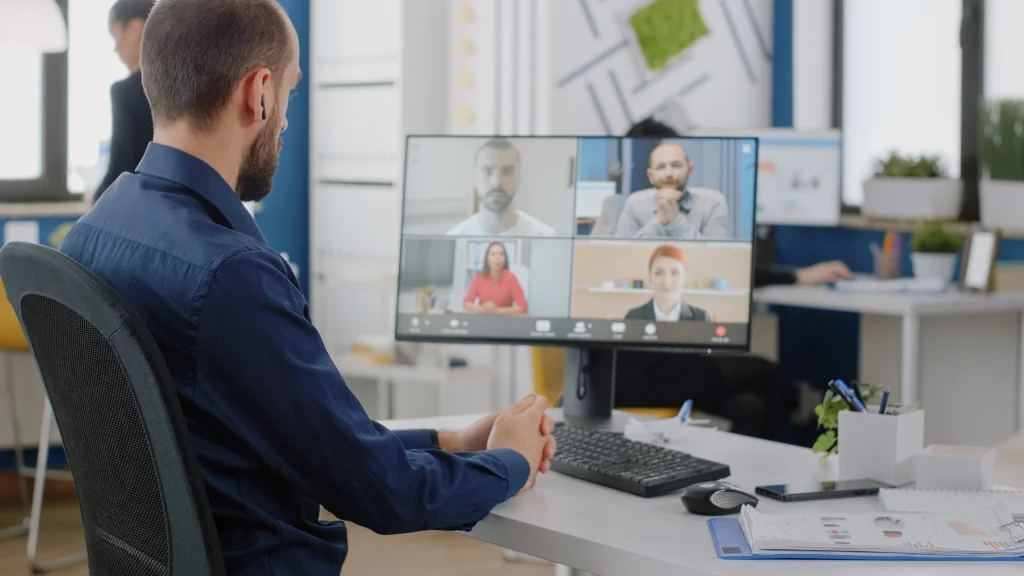 Mann sitzt vor einem PC und nutzt ein Online-Meeting-Tool